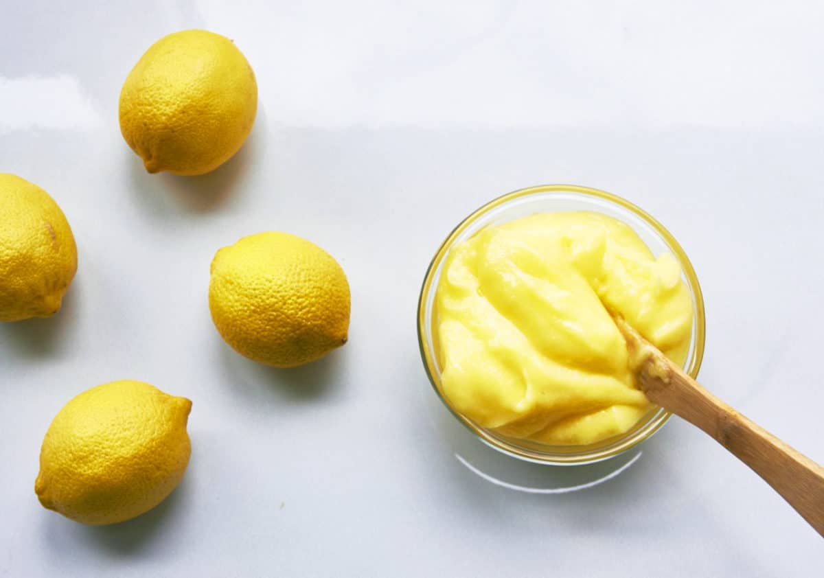 Glass bowl of Lemon Curd on a table with lemons.