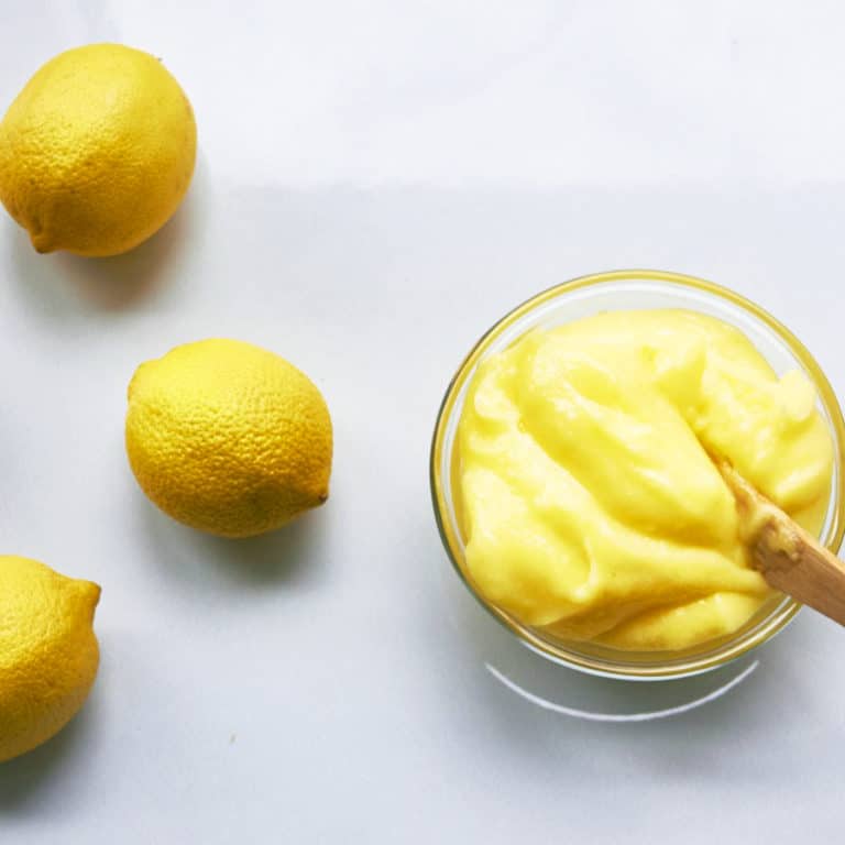 Glass bowl of Lemon Curd on a table with lemons.