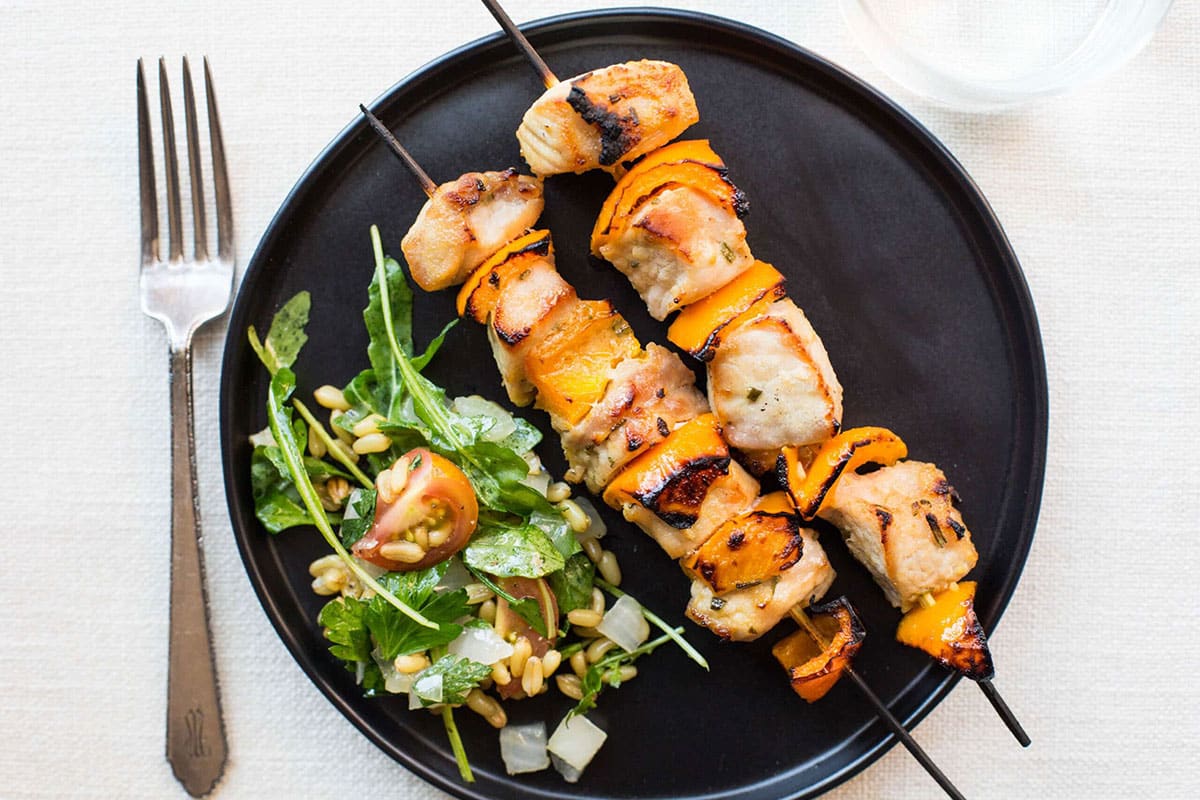 Two Mustard and Maple Pork Kebabs on a black plate with a salad.