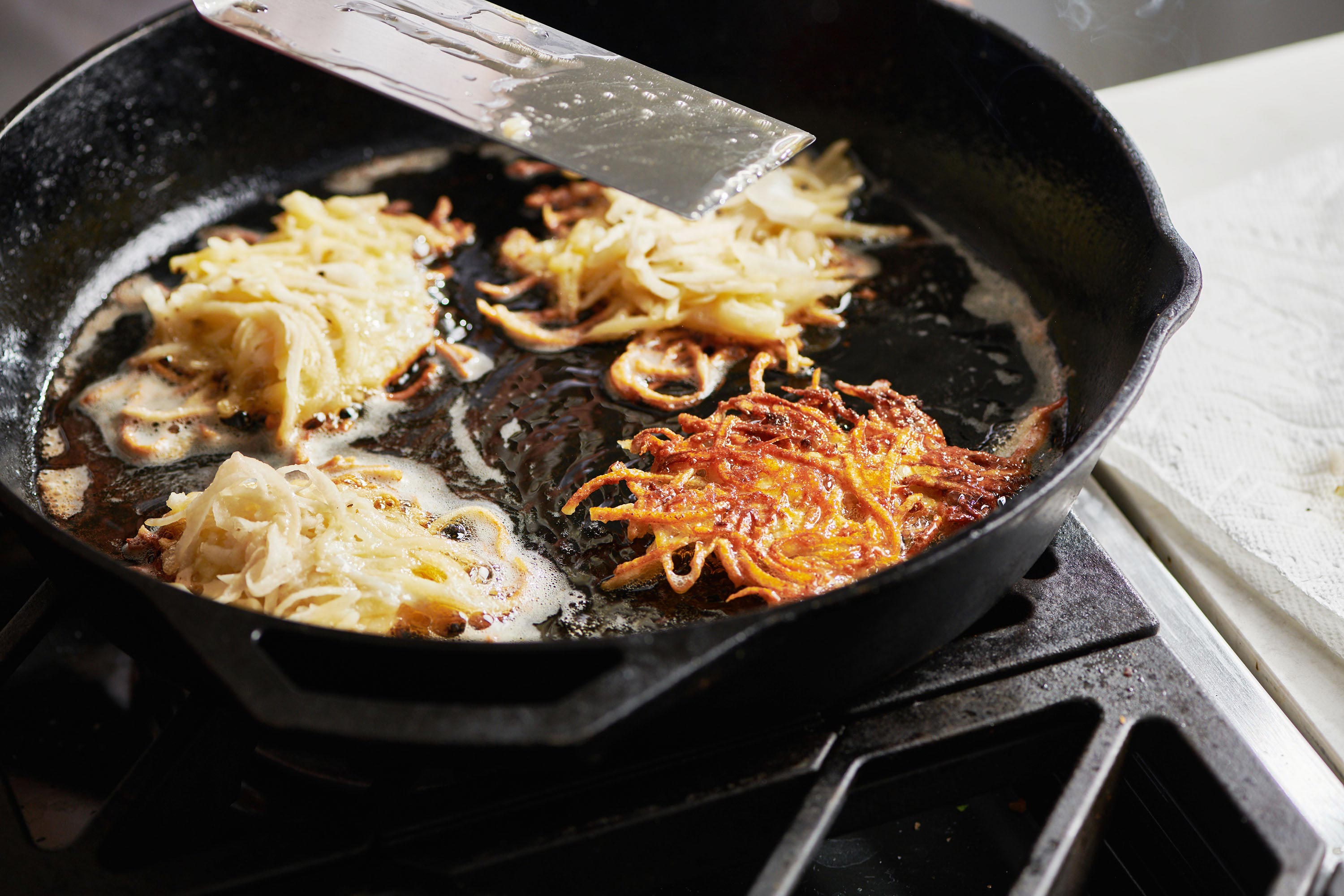 Latkes being cooked in a skillet.