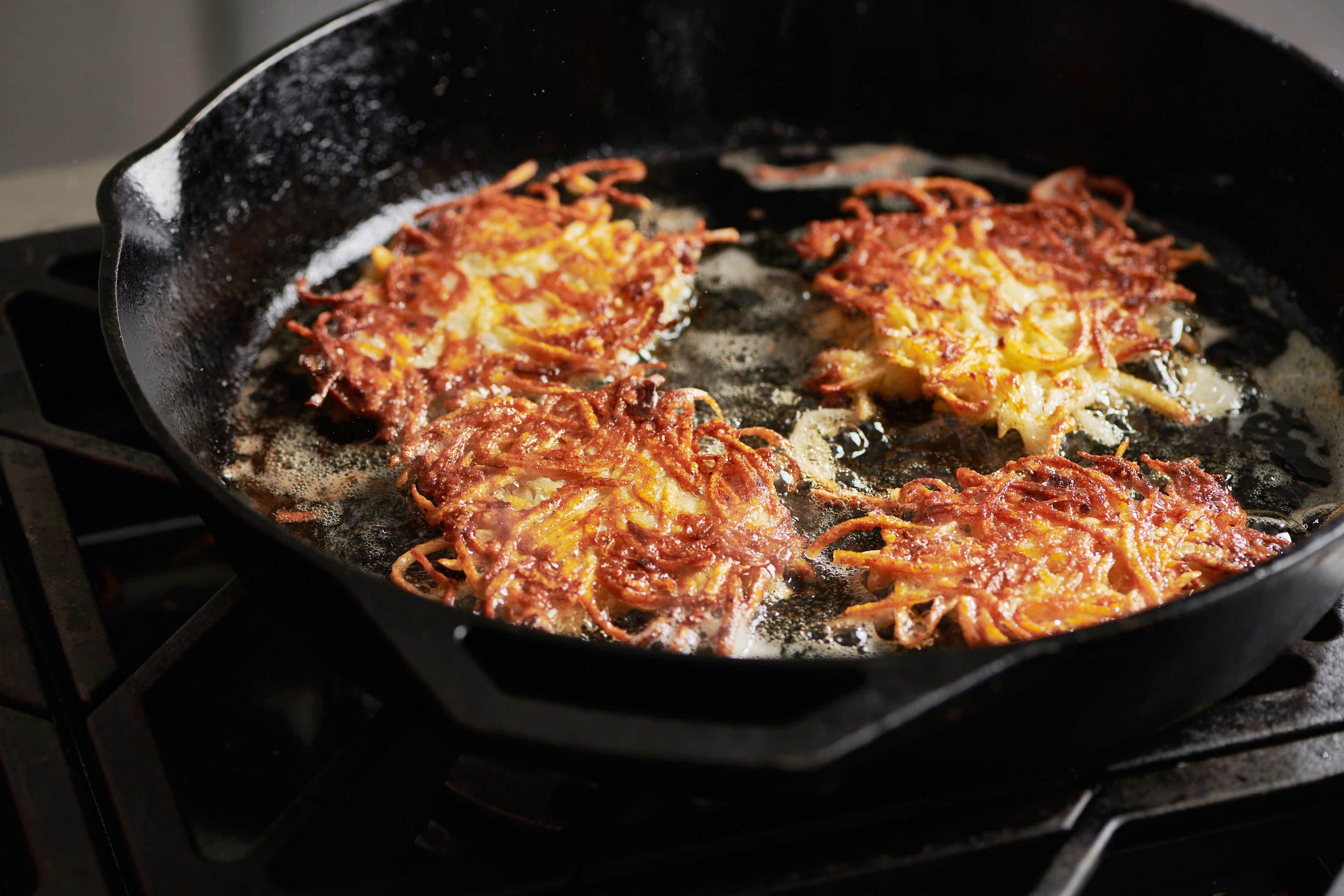 Four latkes frying in a skillet.