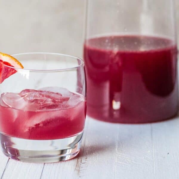 Red cocktail in glass and pitcher on table.