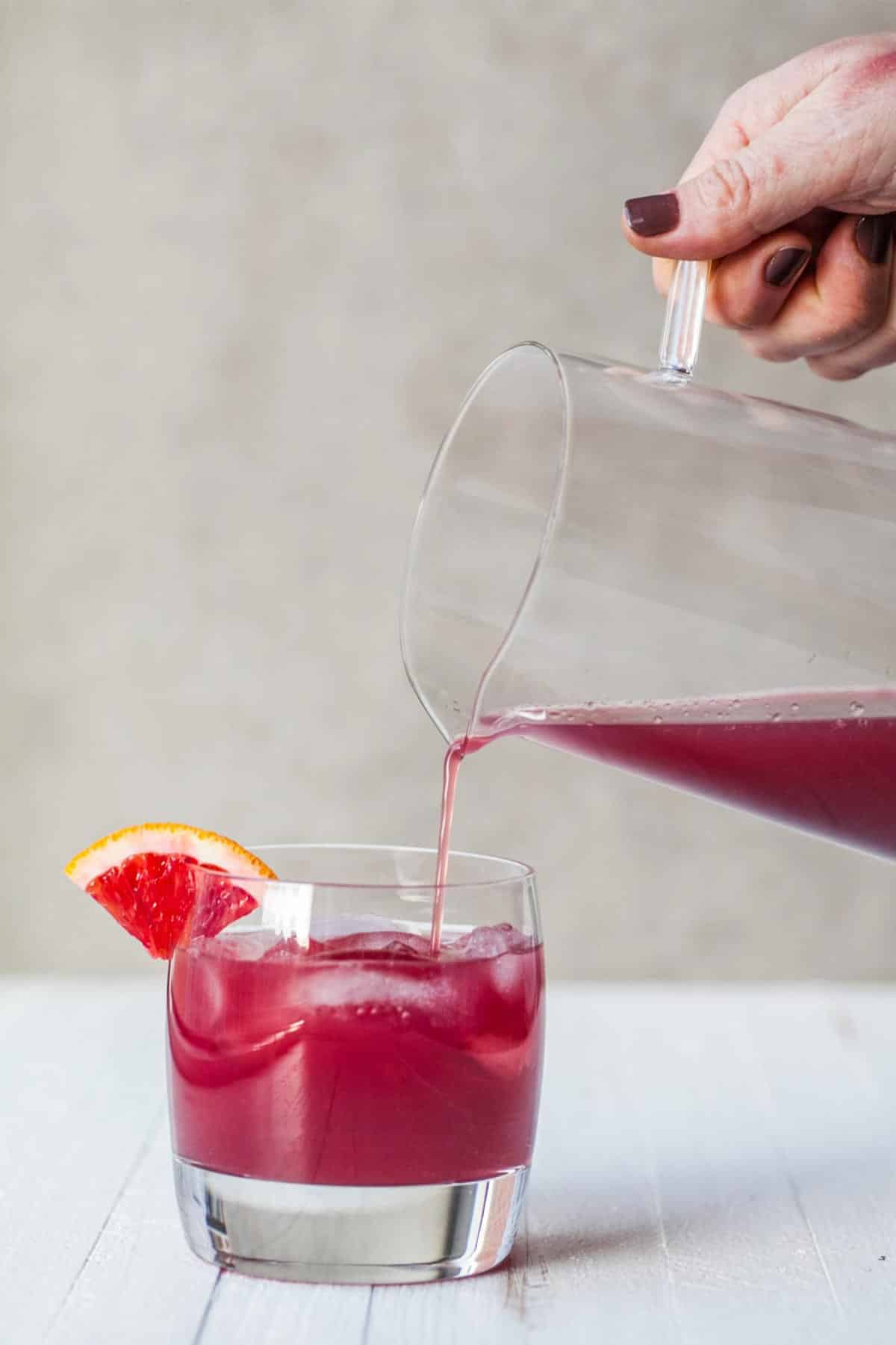 Pouring Red Pomegranate Cocktail from pitcher into glass with a stream of juice.