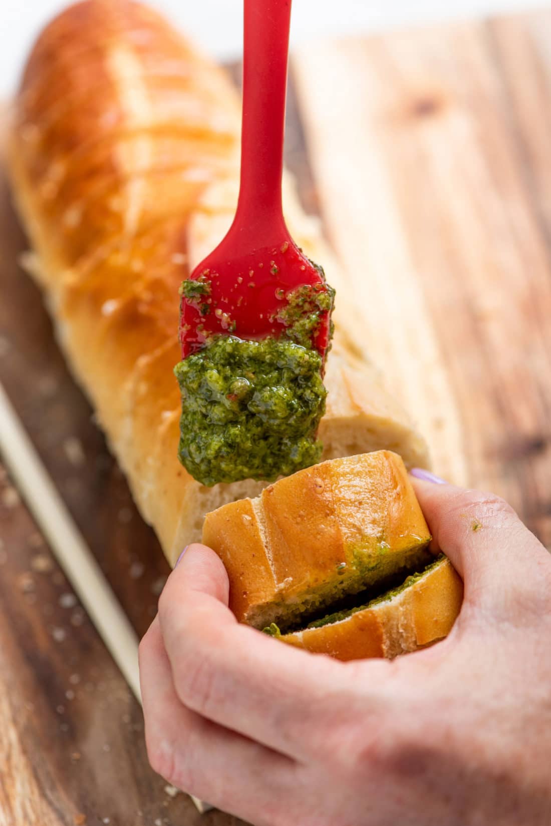 Woman putting Salsa Verde onto partially-sliced bread.