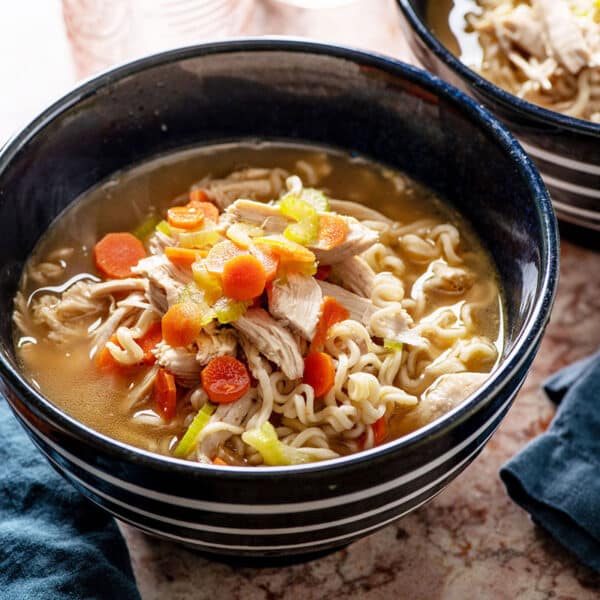 Blue bowl of chicken ramen soup on table with chopsticks.