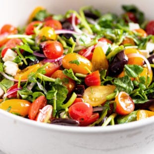 Bowl of colorful Tomato, Red Onion, Watercress, Feta and Olive Salad.