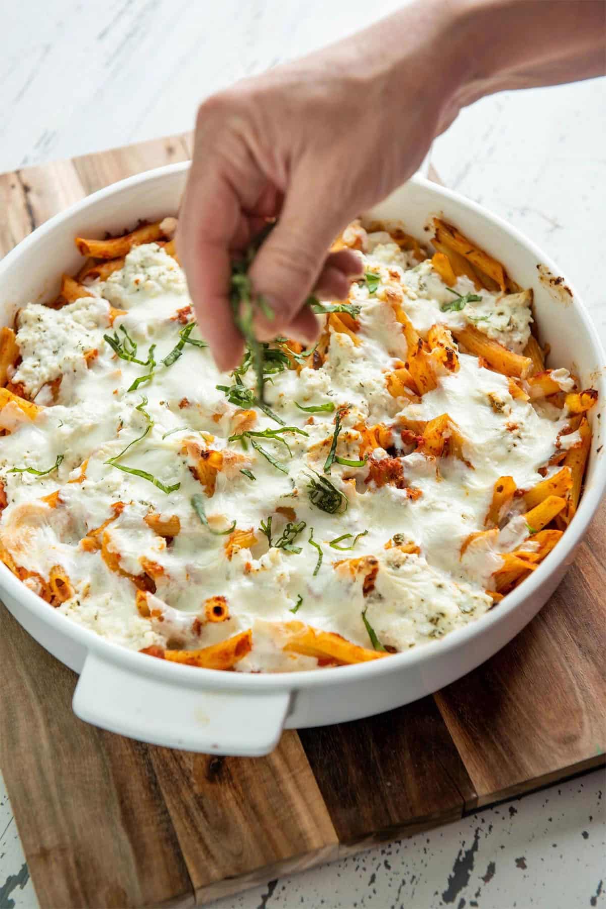 Woman sprinkling thinly-sliced basil onto a dish of Baked Pasta with Bolognese Sauce.