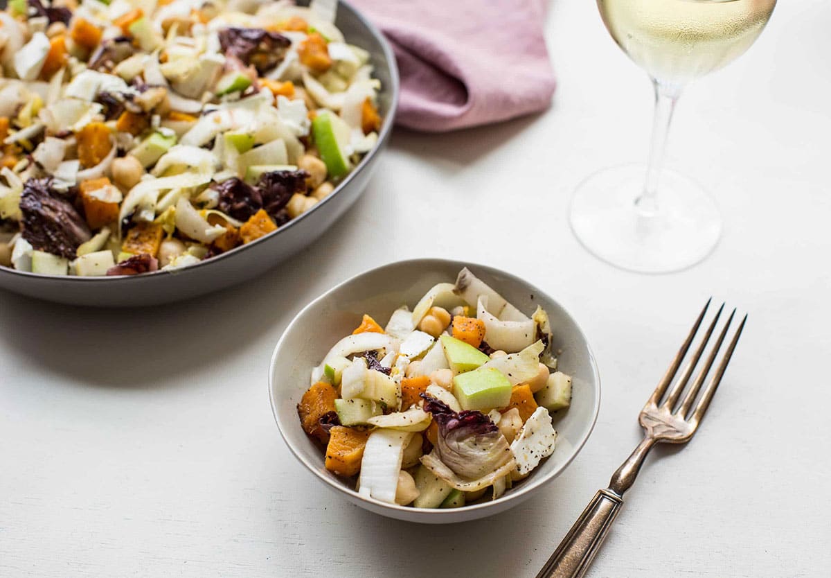 Winter-inspired salad with roasted butternut squash, radicchio, and other ingredients in bowls on table.
