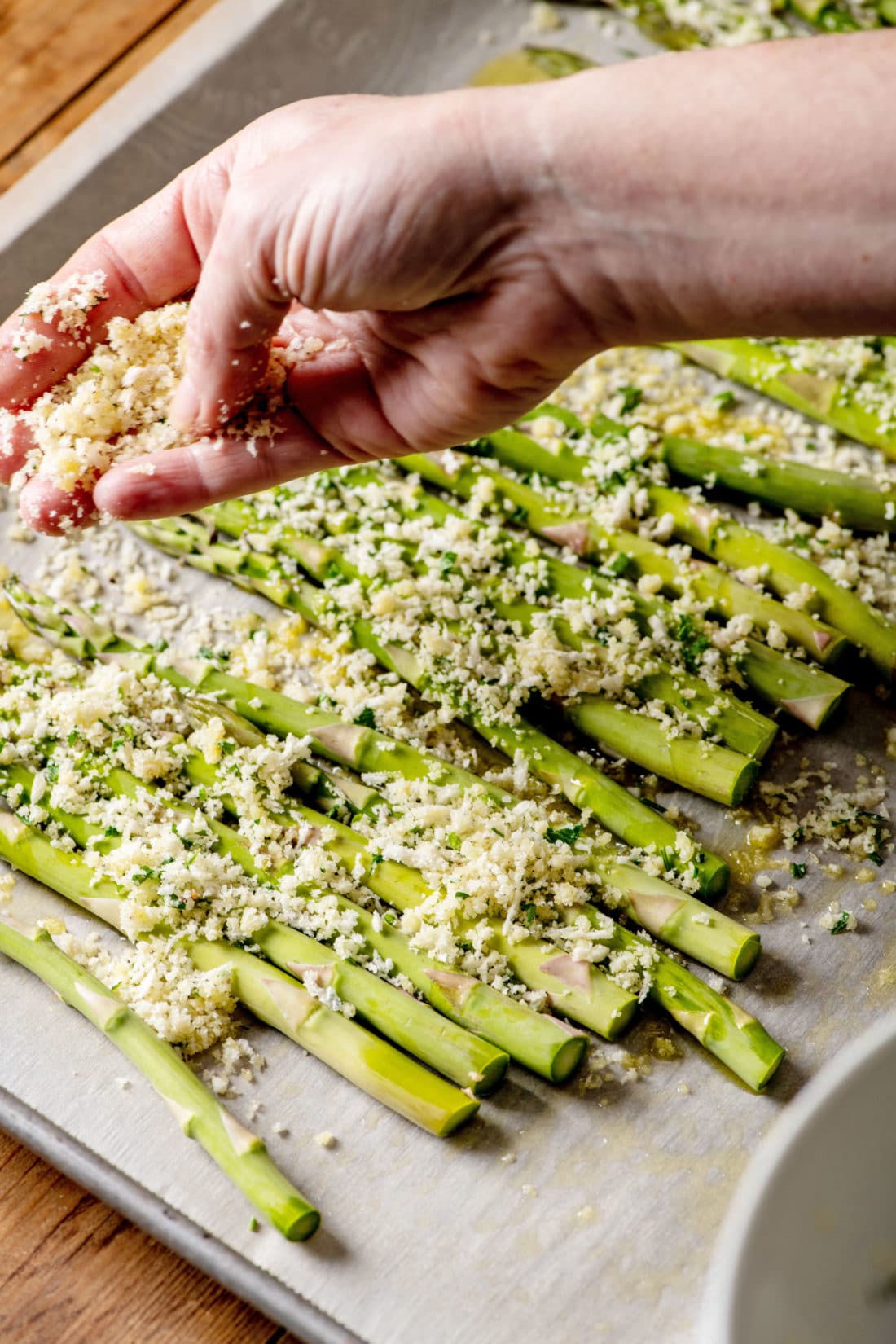 Spreading panko over asparagus on a baking sheet