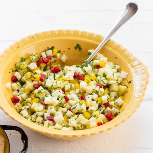 Yellow bowl with Pineapple Mint Jalapeno Salsa on table with chips and drinks.