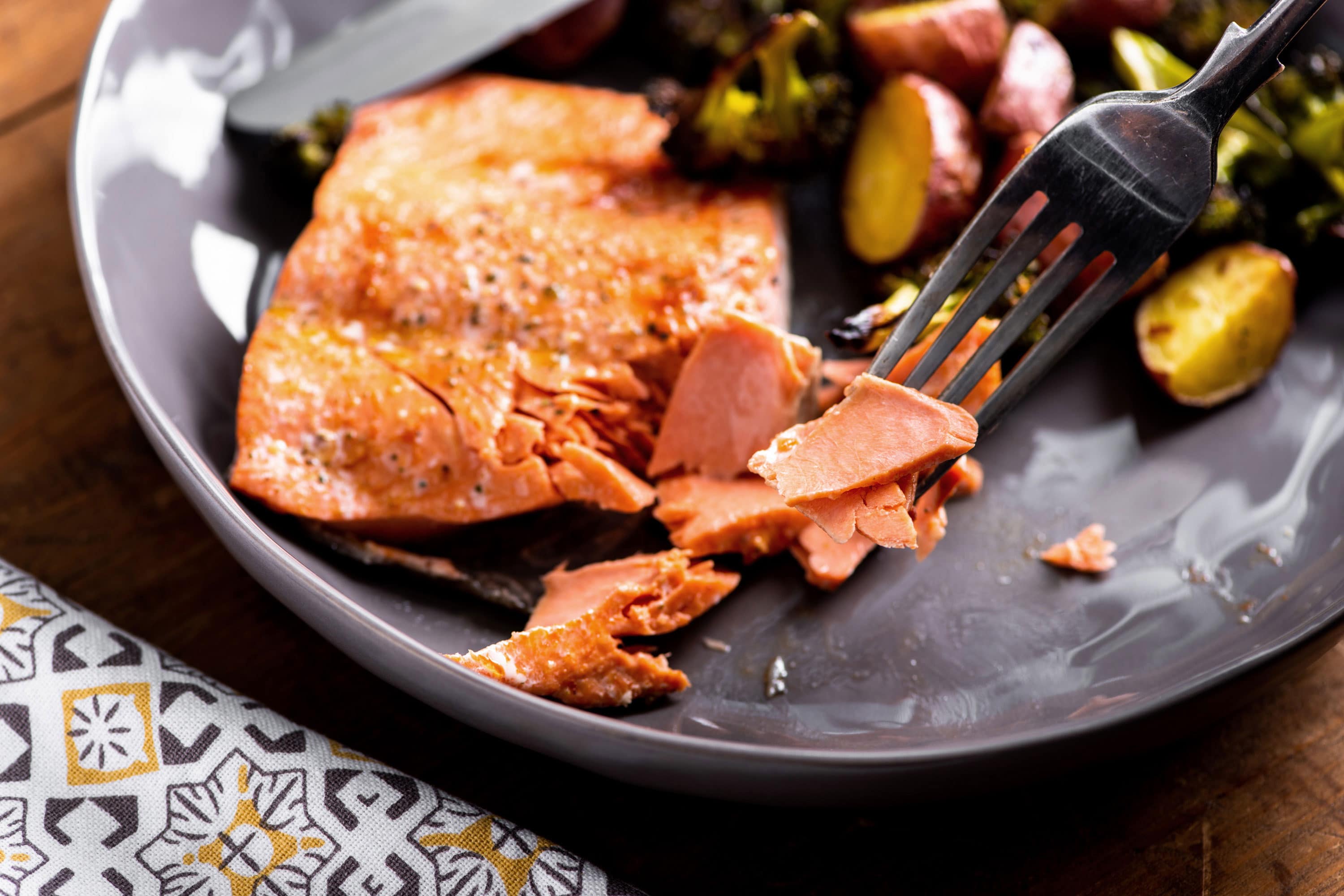 Fork flaking salmon on a gray plate.