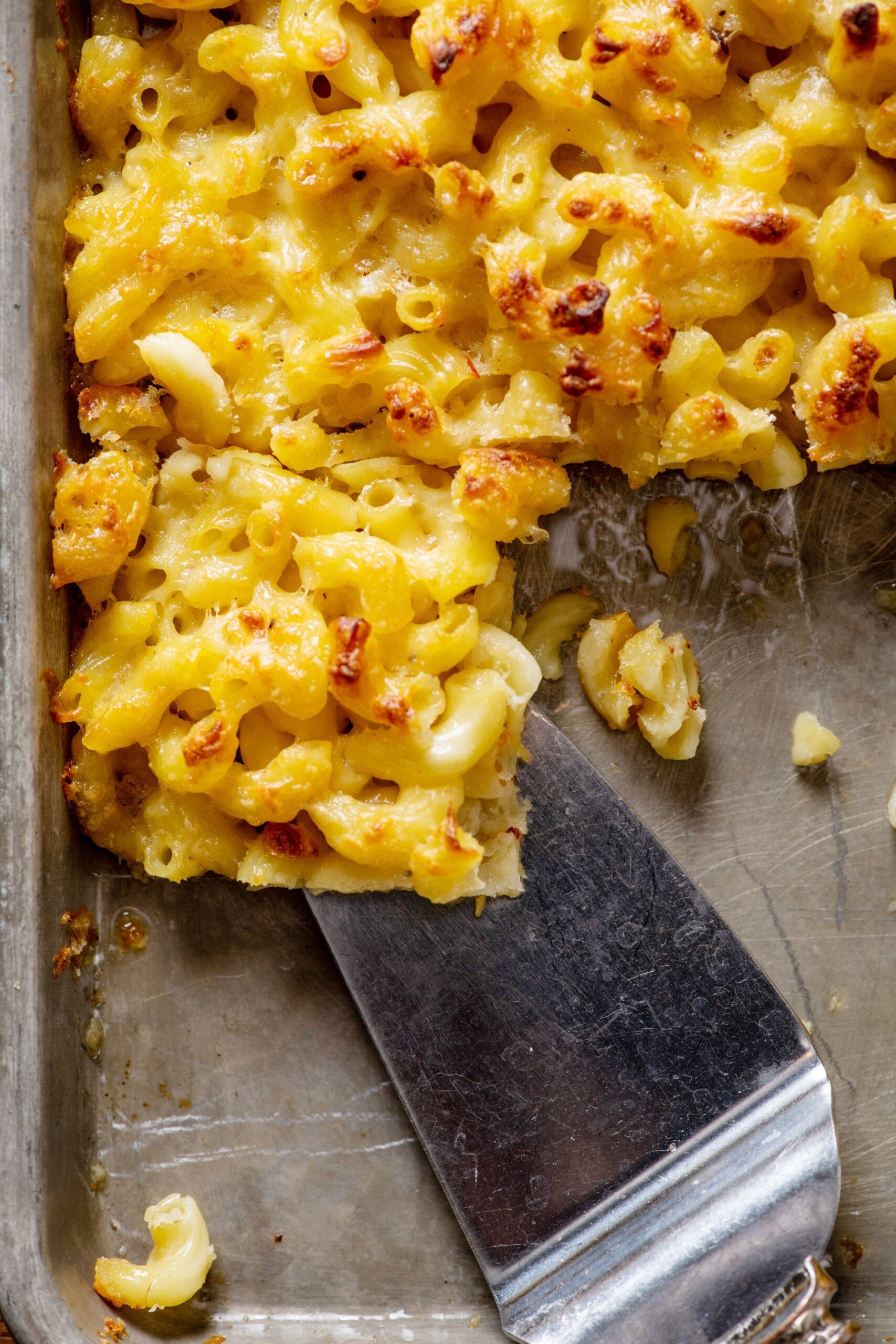 Spatula grabbing a Sheetpan Macaroni and Cheese Square from a baking pan.