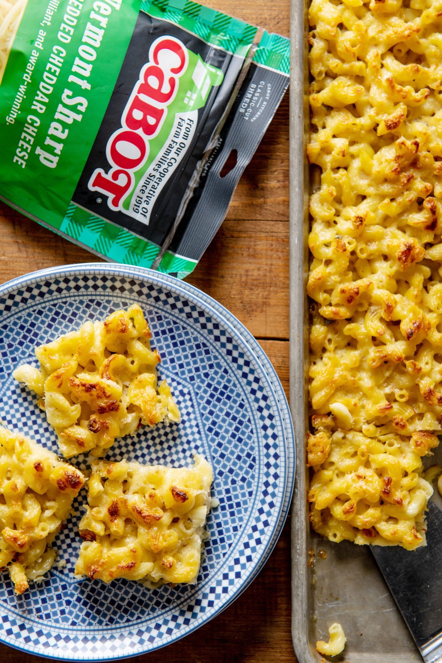 Plate of Macaroni and Cheese Squares next to a sheetpan and a bag of Cabot cheese.