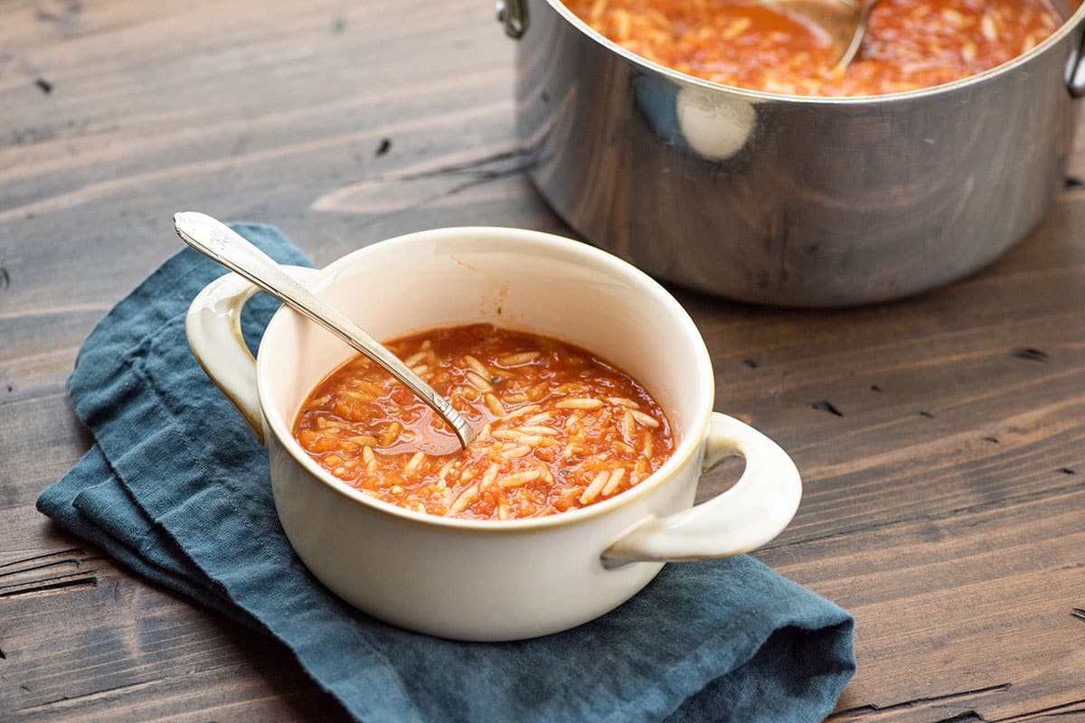 Tomato, Orzo and Dill Soup in white bowl with a spoon.