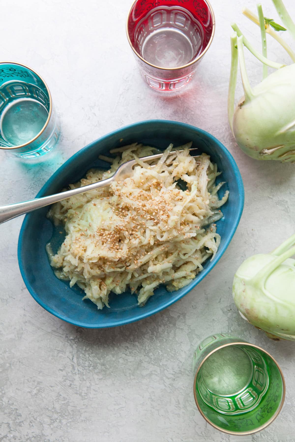 Asian Kohlrabi and Apple Slaw in a blue bowl with a serving fork with whole kohlrabi nearby.