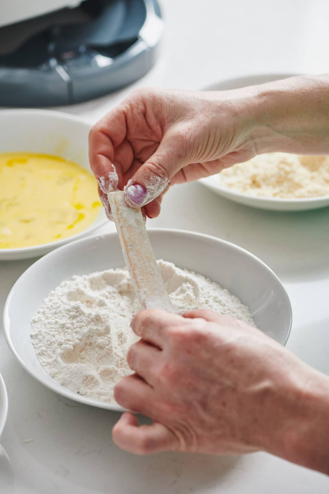 Woman coating a cheese stick in flour.