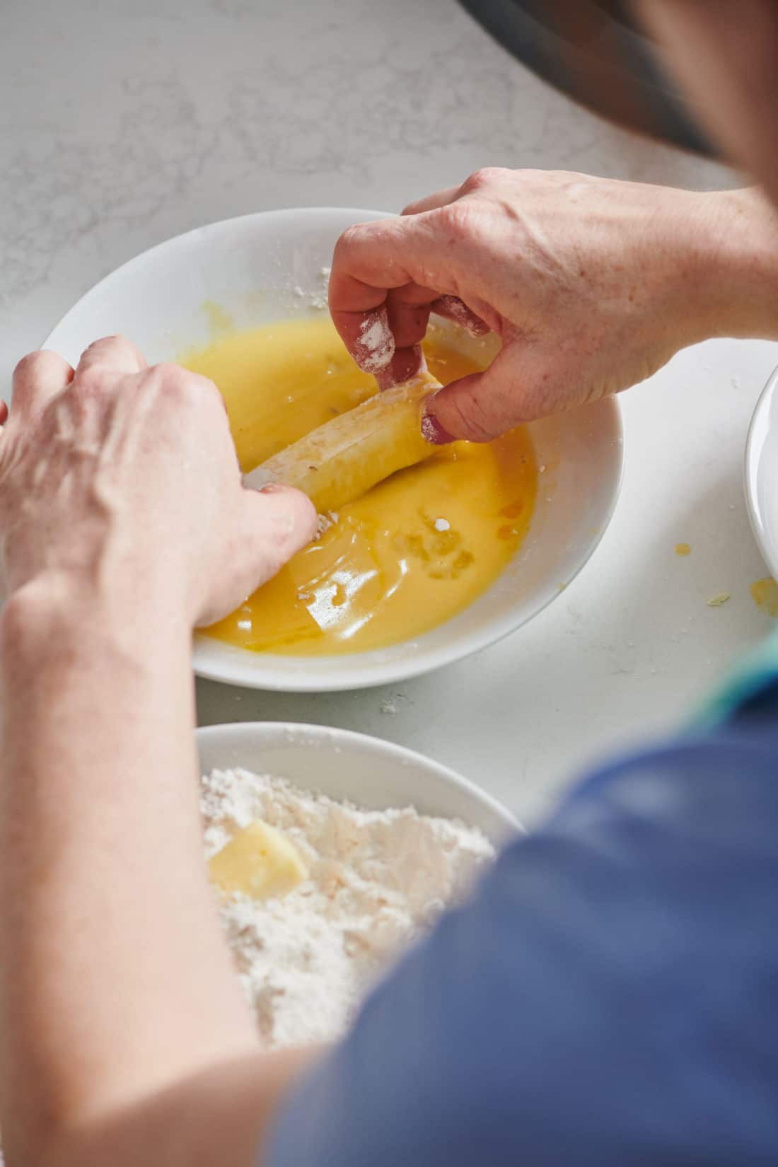 Woman rolling a cheese stick in an egg mixture.