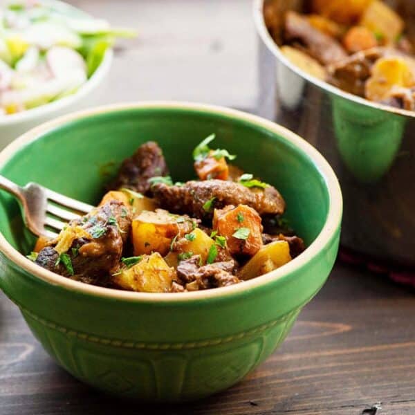 Apple cider beef stew in green bowl on table.