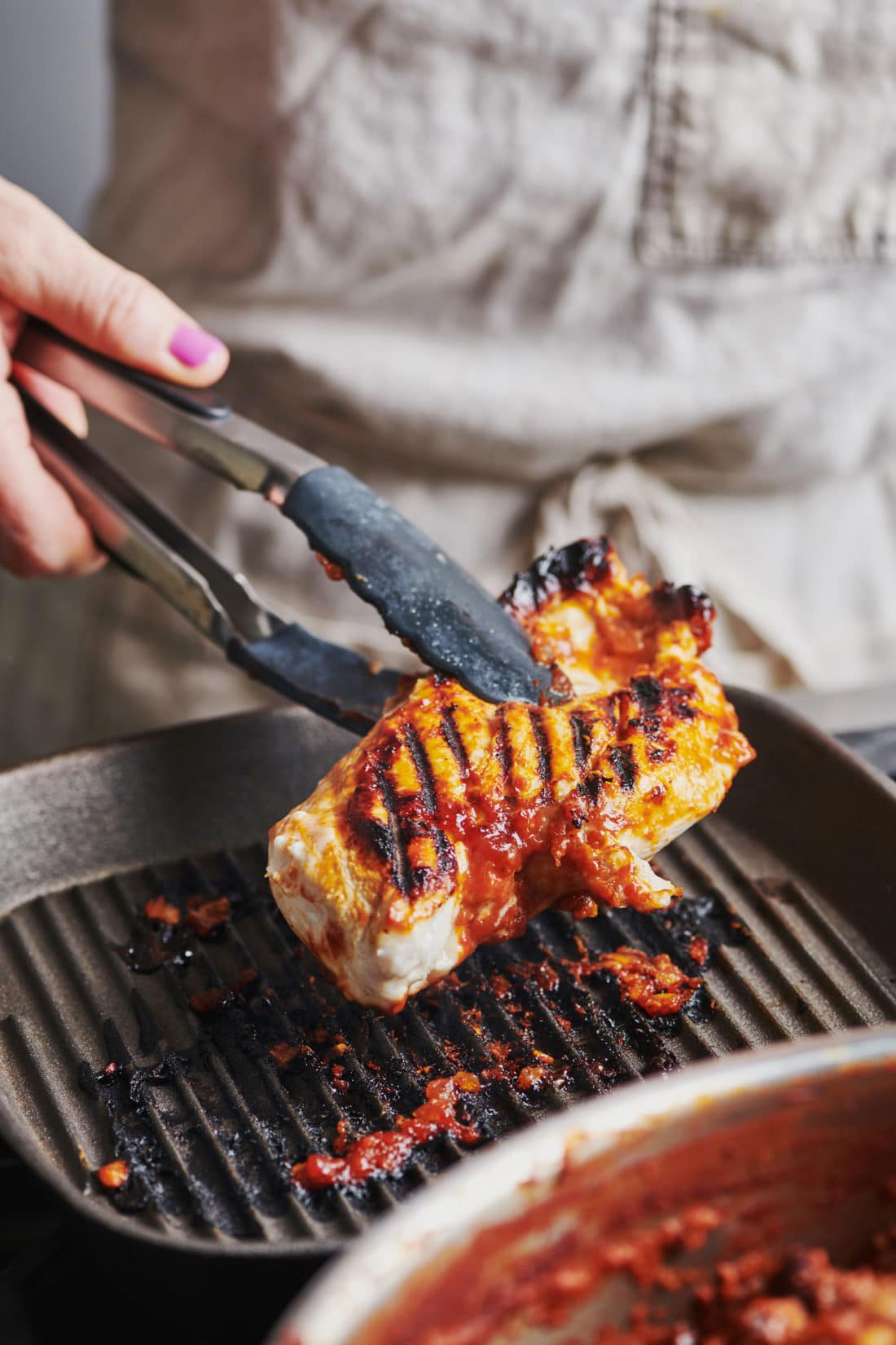 Tongs flipping chicken on a grill pan.