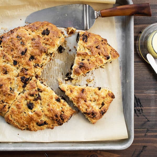 Golden brown dried cherry scone on parchment-lined pan with knives.