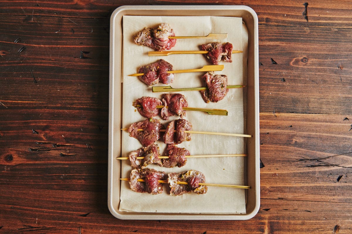 Lined baking sheet of Lamb Satay skewers.