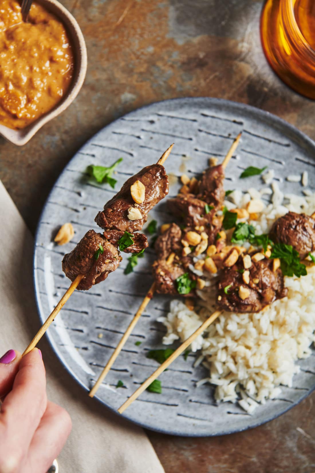 Woman holding a Lamb Satay skewer.