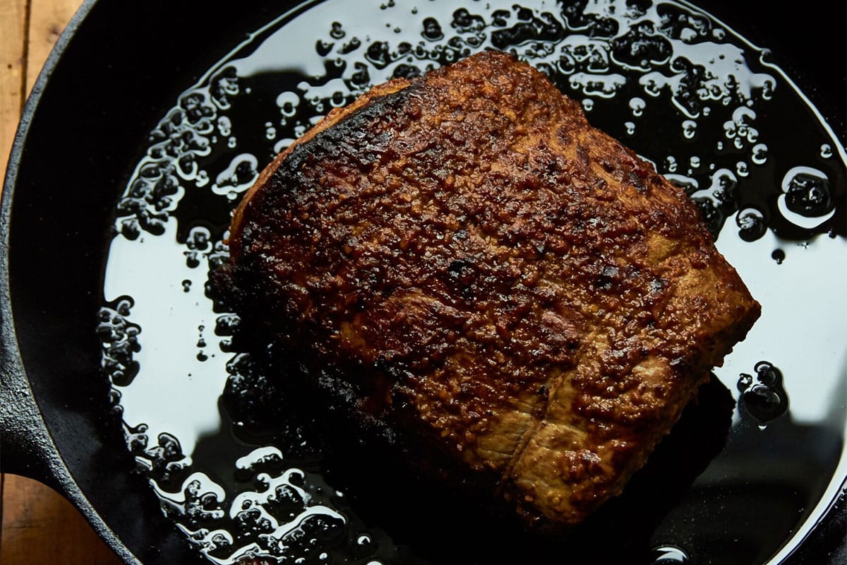 Mustard-crusted roast beef in cast-iron pan on table.