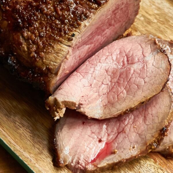 Partially sliced roast beef with mustard and garlic crust on wood cutting board.