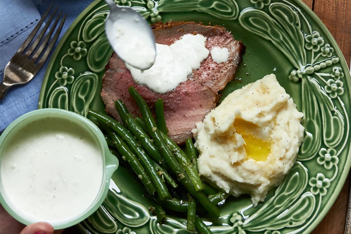 Woman drizzling Horseradish sauce onto Roast Beef with Mustard Garlic Crust.