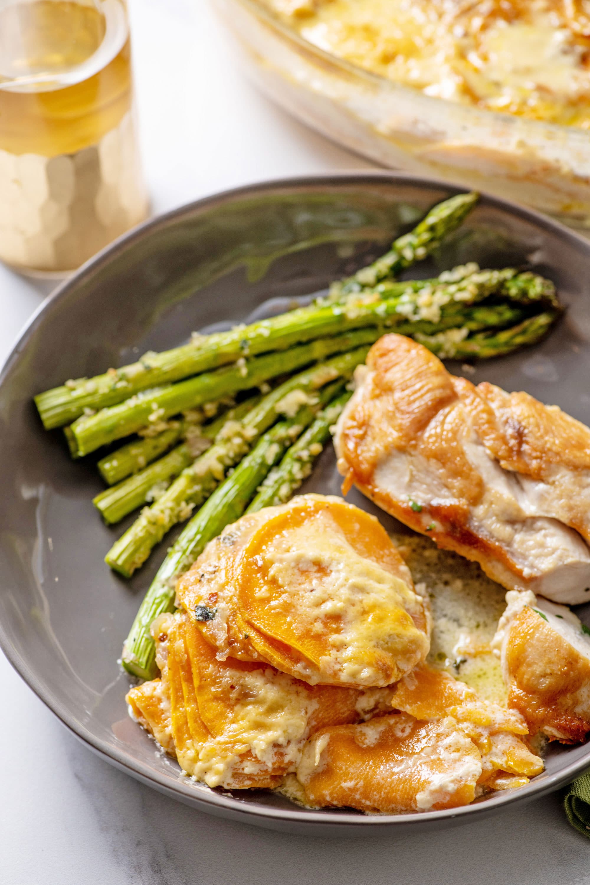 Scalloped Sweet Potatoes on a gray dish with chicken and asparagus.
