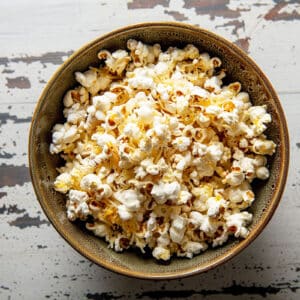 Homemade stovetop popcorn with cheddar cheese in bowl on wood table.