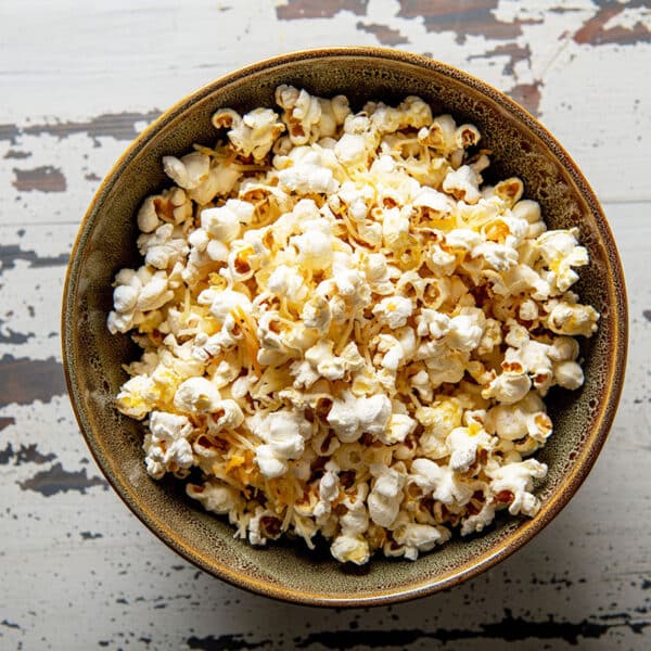Homemade stovetop popcorn with cheddar cheese in bowl on wood table.