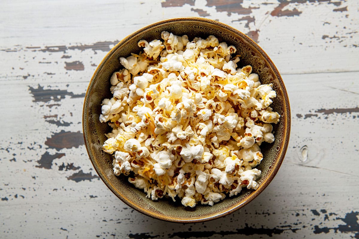 Homemade stovetop popcorn with cheddar cheese in bowl on wood table.