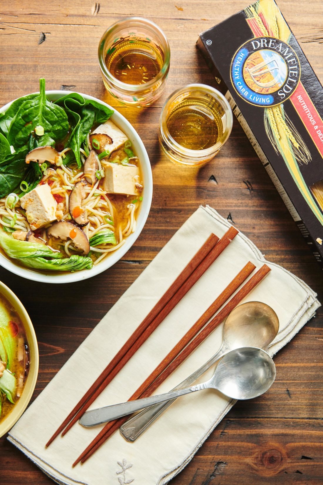 Chopsticks and spoons with bowls of Angel Hair “Ramen” with Mushrooms, Tofu, Bok Choy, and Scallions.