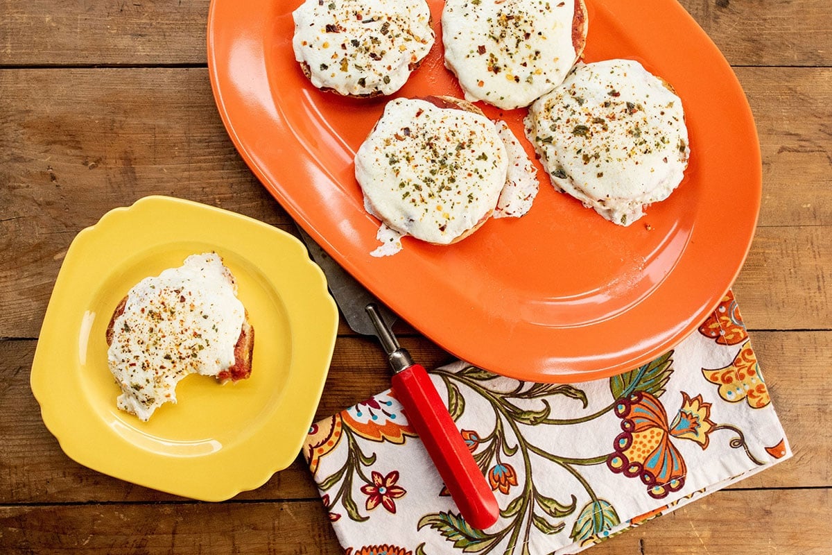 English Muffin Pizza on a stack of colorful plates.