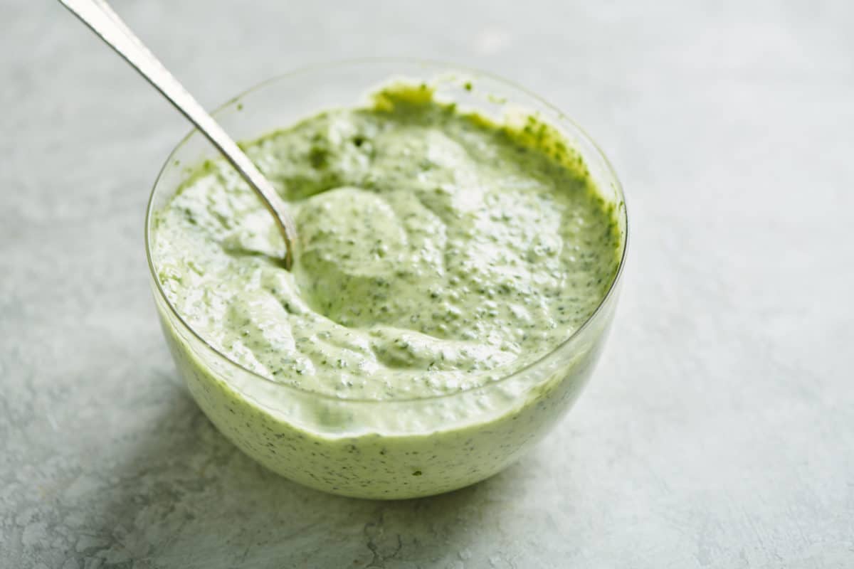 Green, Herbed Mayonnaise in a glass bowl with a spoon.