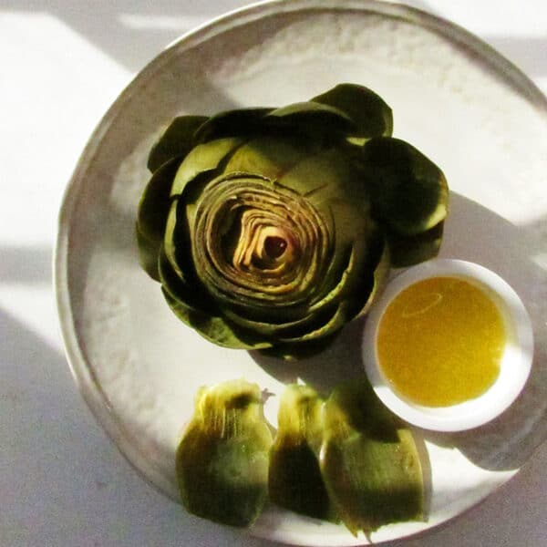 Steamed artichoke on plate with melted butter sauce.