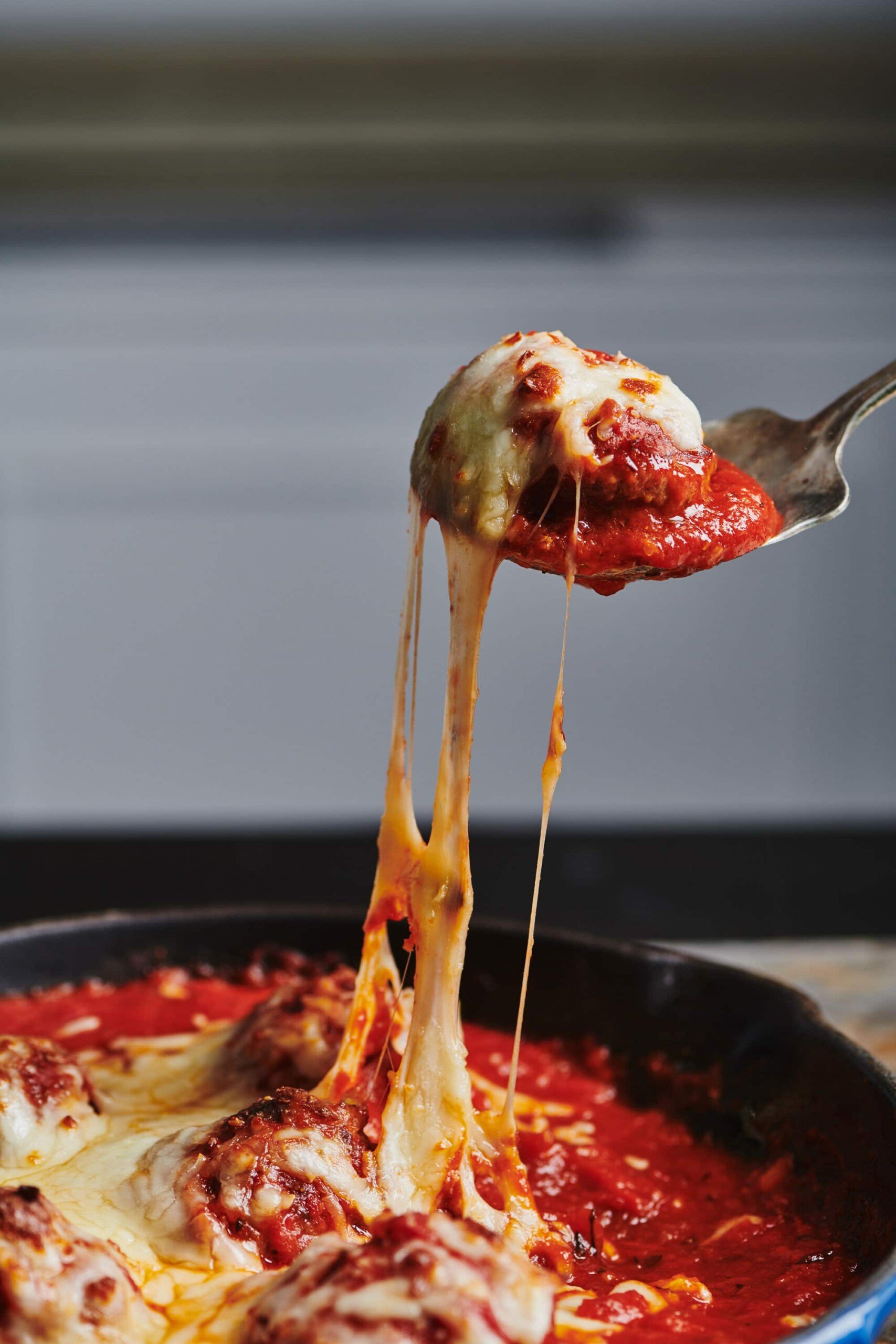 Spoon grabbing a Meatball with melted cheese.