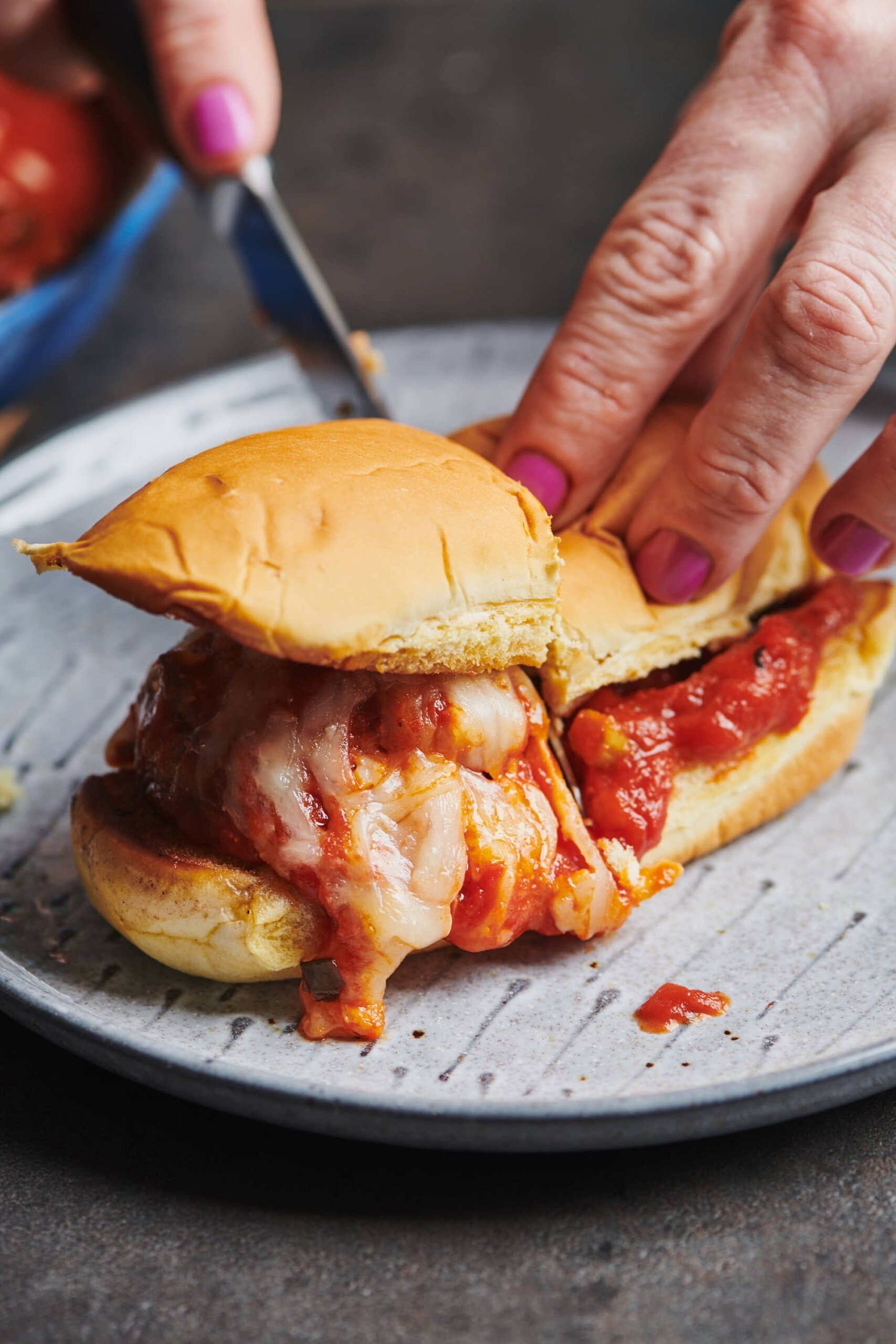 Woman cutting a Meatball Sub with a knife.