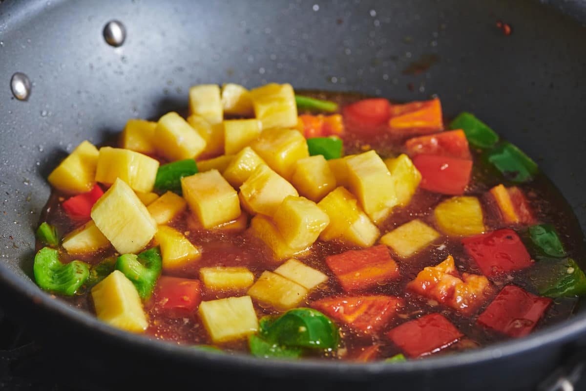 Pineapple, peppers, and sweet and sour sauce in a pan.