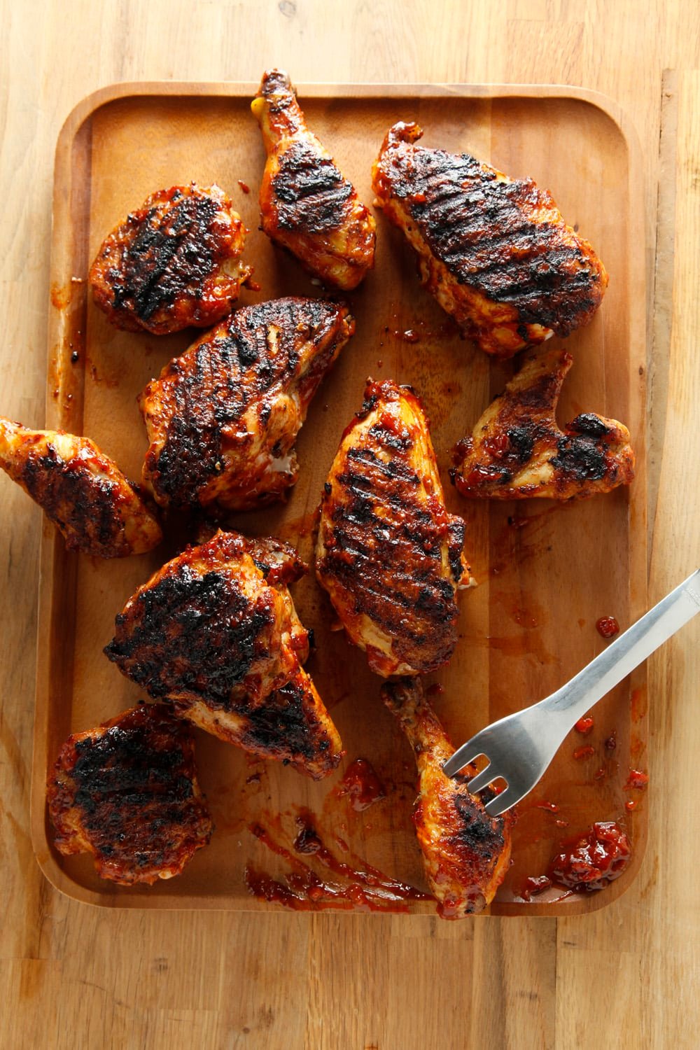 Fork sticking out of a barbequed chicken leg on a wooden surface.