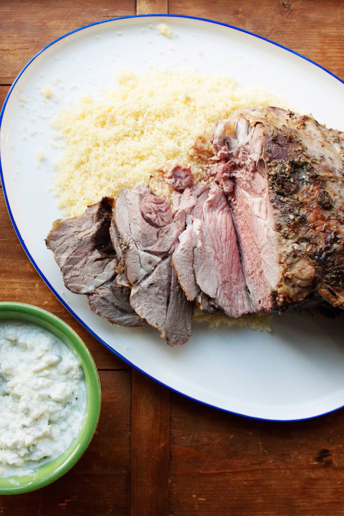 Partially-sliced Slow Cooked Mediterranean Leg of Lamb with Tzatziki on a platter.