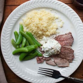 Plate with couscous, peas, and slices of Mediterranean Leg of Lamb with Tzatziki.