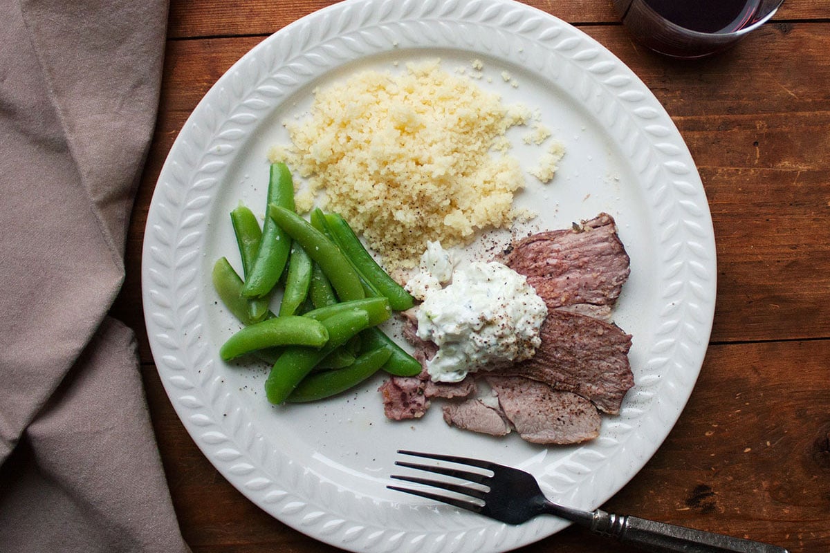 Plate with couscous, peas, and slices of Mediterranean Leg of Lamb with Tzatziki.