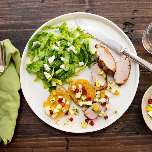 Sliced pork tenderloin on plate with salad and fried green tomatoes.