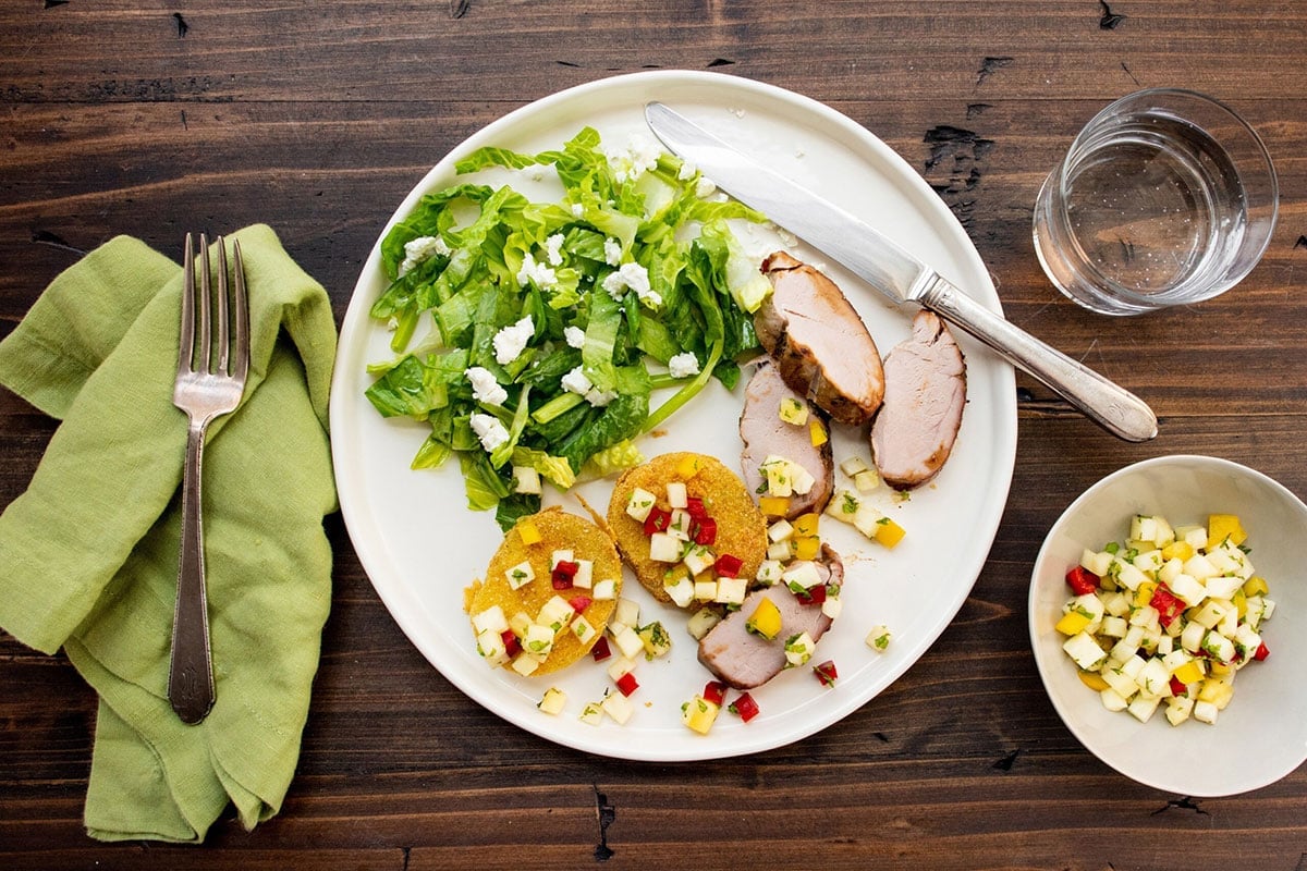 Sliced pork tenderloin on plate with salad and fried green tomatoes.