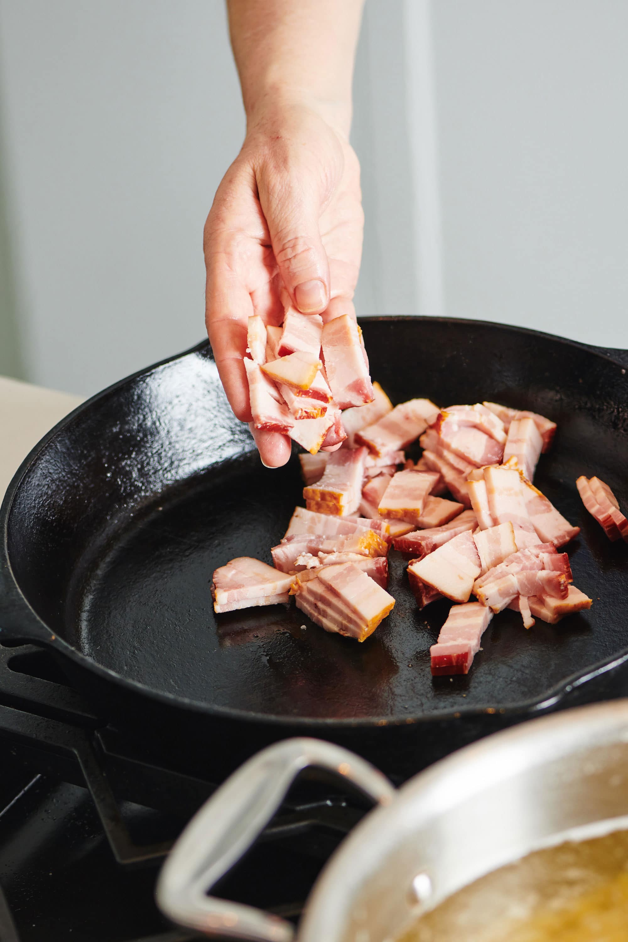 Woman putting uncooked sliced bacon into a cast iron pan.