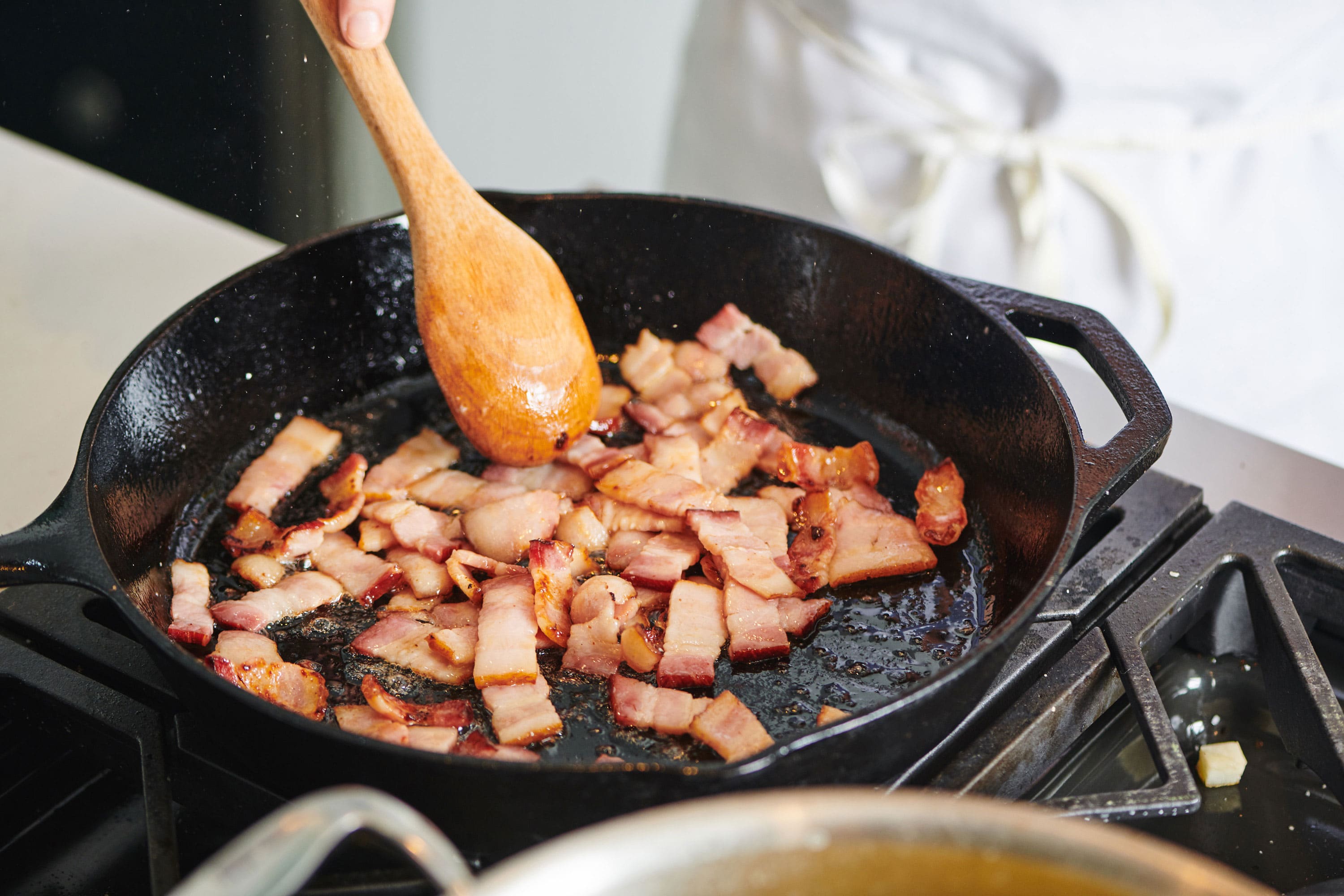 Spoon stirring Bacon Lardons in a cast iron pan.