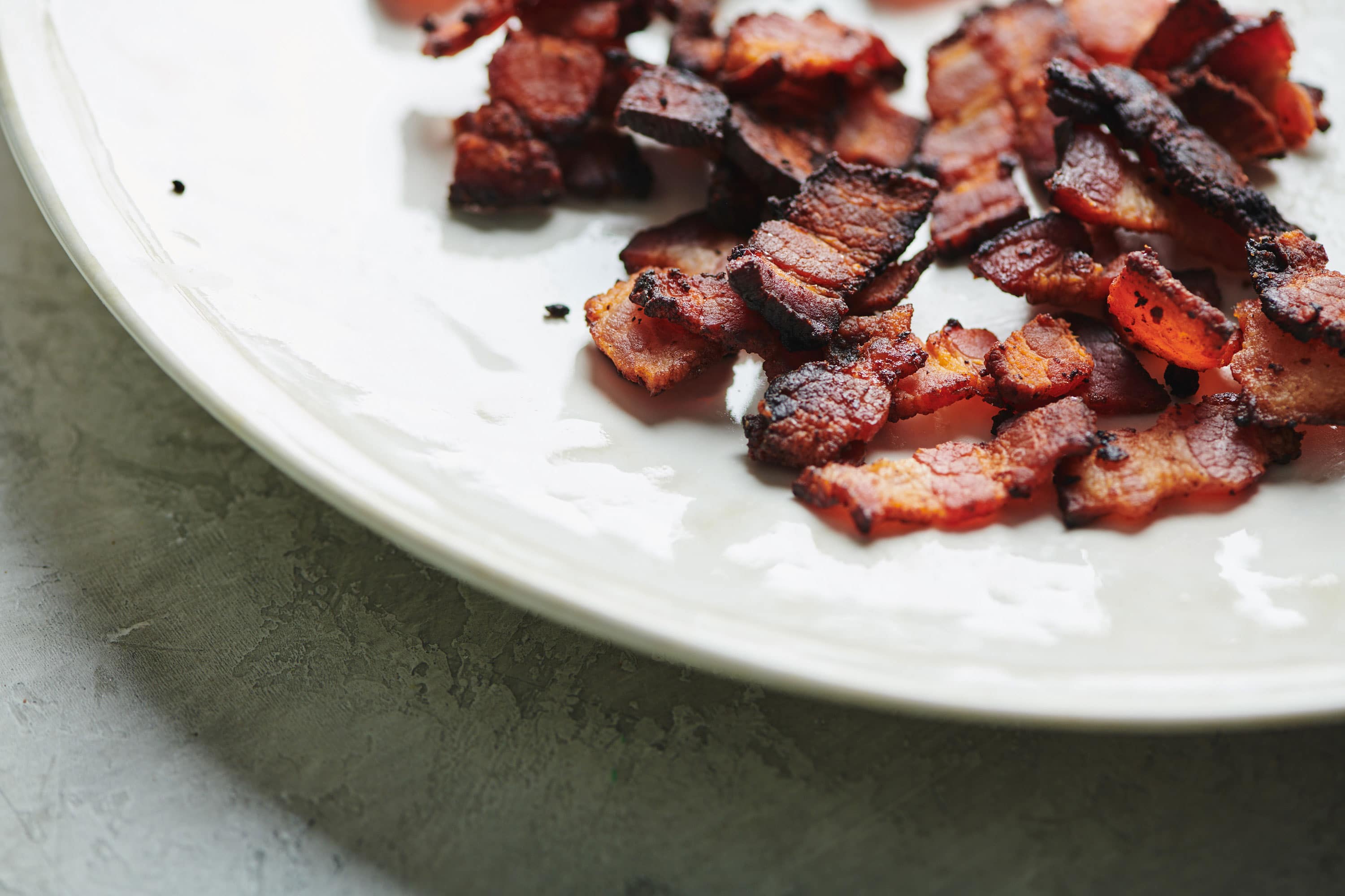 Cooked Bacon Lardons on a white plate.