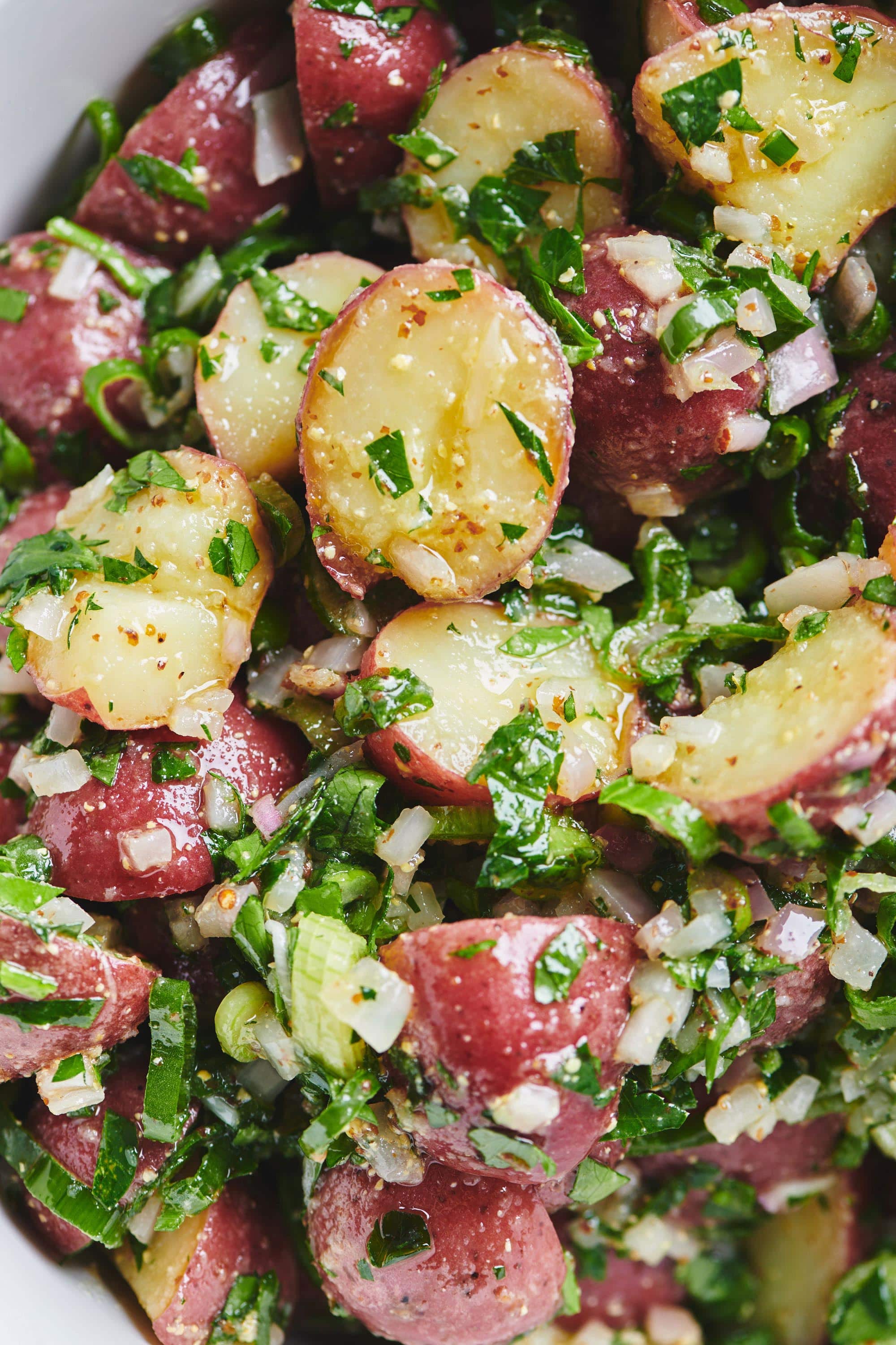Potato salad in bowl topped with scallions and parsley.